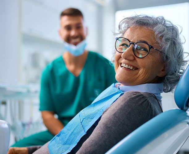 Smiling patient sitting in treatment chair next to dentist