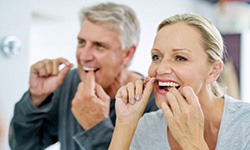 Smiling couple flossing in bathroom together