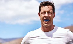 Man in white shirt wearing blue mouthguard outside