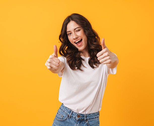 Woman in white t-shirt giving two thumbs up with yellow background