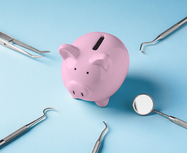 A piggy bank surrounded by dental instruments on a light blue background