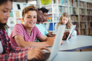 Highschool smiling while classmates study on their laptops in a library