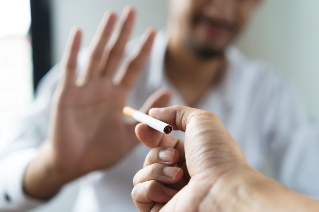 Man blurry in background holding hand up to turn down a cigarette being offered